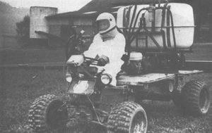 Ein Mann im weißen Schutzanzug mit Helm fährt ein Quad mit aufgesattelter Pflanzenschutzspritze.