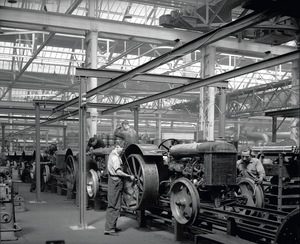 Ein Arbeiter am Band der amerikanischen Fordson-Werke montiert ein Hinterrad des Traktors.